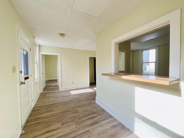 spare room featuring a baseboard radiator, baseboards, wood finished floors, and a paneled ceiling