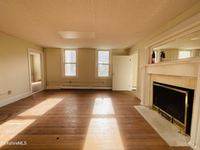unfurnished living room with a baseboard heating unit, a tiled fireplace, baseboards, and hardwood / wood-style flooring