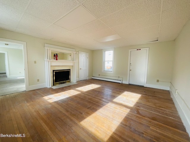 unfurnished living room with a baseboard heating unit, baseboards, hardwood / wood-style floors, and a fireplace with flush hearth