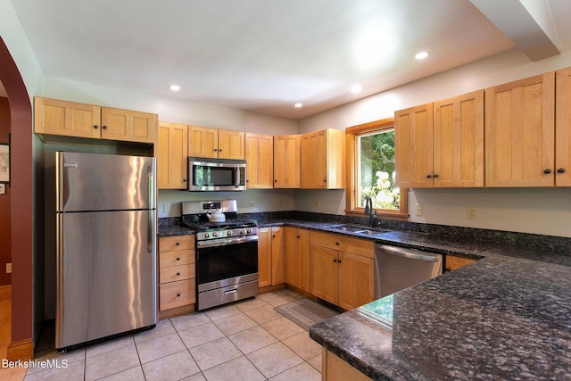 kitchen with light tile patterned floors, sink, stainless steel appliances, and dark stone counters