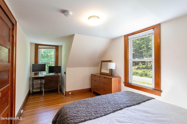 bedroom featuring a baseboard radiator, hardwood / wood-style flooring, and vaulted ceiling