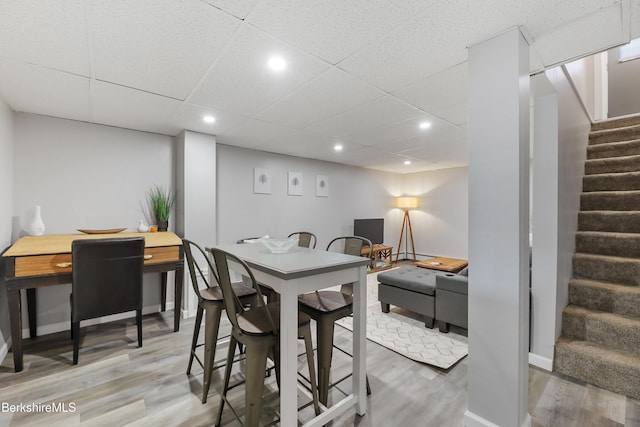 dining room featuring stairs, wood finished floors, baseboards, a drop ceiling, and recessed lighting