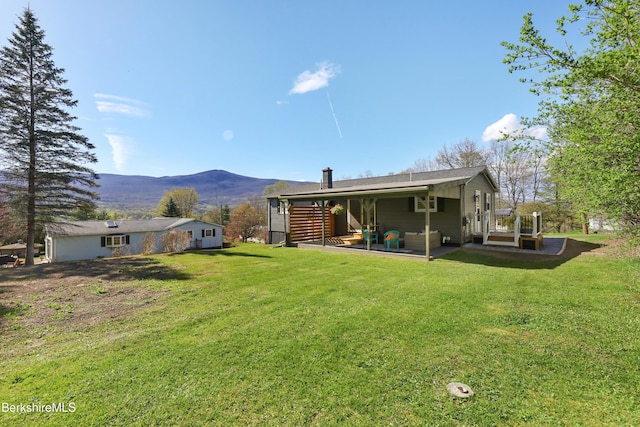 back of property featuring a lawn, a mountain view, and a patio