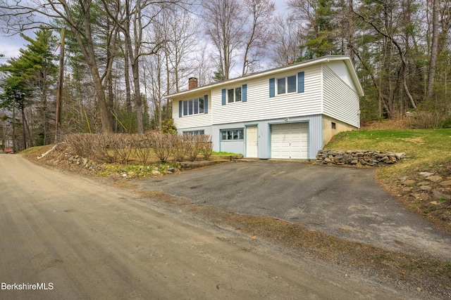view of front facade with an attached garage, a chimney, and aphalt driveway