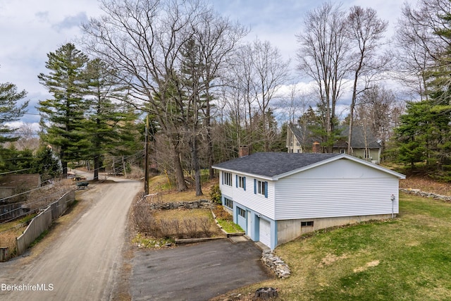 view of side of home with a chimney, roof with shingles, aphalt driveway, a yard, and an attached garage