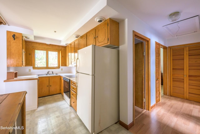 kitchen featuring a sink, light countertops, freestanding refrigerator, light floors, and range with electric stovetop
