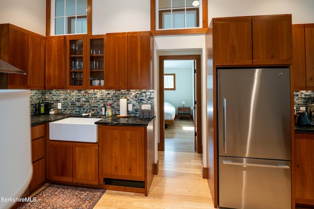 kitchen featuring light wood-style flooring, glass insert cabinets, freestanding refrigerator, a sink, and backsplash