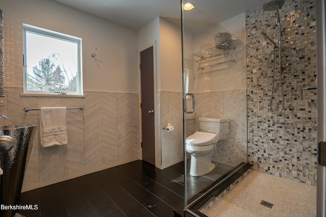 bathroom with toilet, a wainscoted wall, a shower stall, and tile walls