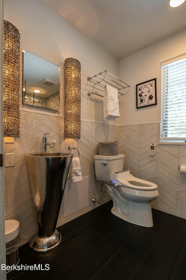 bathroom featuring toilet, wood finished floors, tile walls, and wainscoting