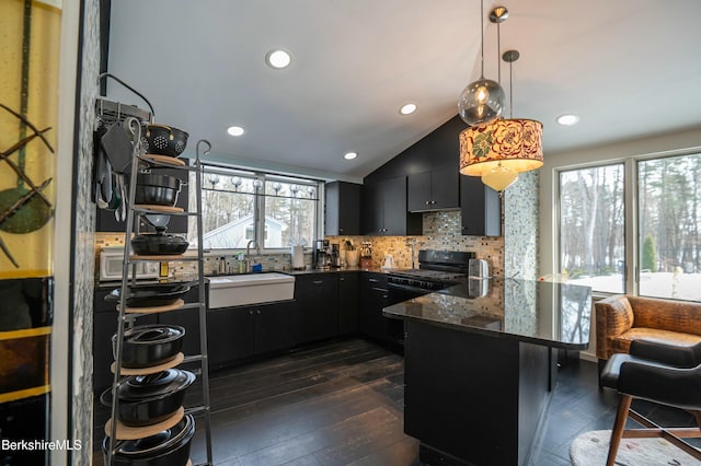 kitchen with black range with gas cooktop, a peninsula, a sink, dark cabinetry, and backsplash