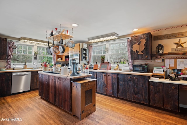 kitchen with dark brown cabinets, a center island, light wood-type flooring, and appliances with stainless steel finishes