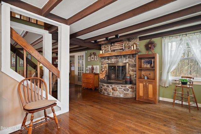 living room featuring beamed ceiling, a stone fireplace, and hardwood / wood-style floors