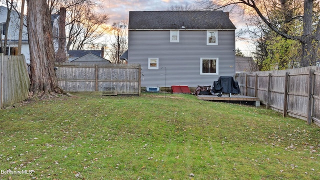 back house at dusk with a lawn and a deck