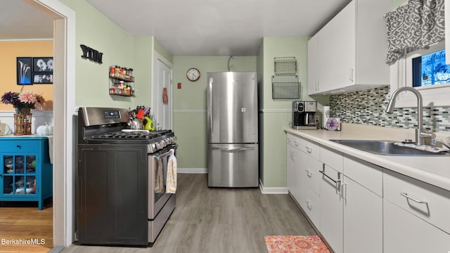 kitchen featuring tasteful backsplash, white cabinetry, sink, stainless steel appliances, and light hardwood / wood-style flooring