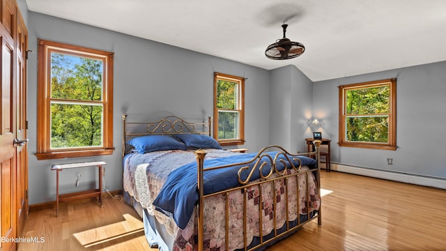 bedroom with multiple windows, a baseboard heating unit, and light wood-type flooring