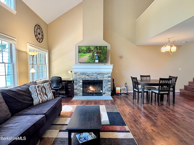 living room with a notable chandelier, dark hardwood / wood-style floors, a stone fireplace, and high vaulted ceiling