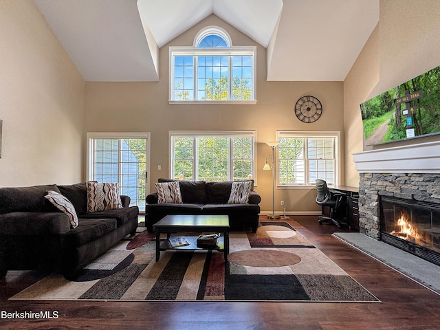 living room with a stone fireplace, a towering ceiling, and dark hardwood / wood-style floors