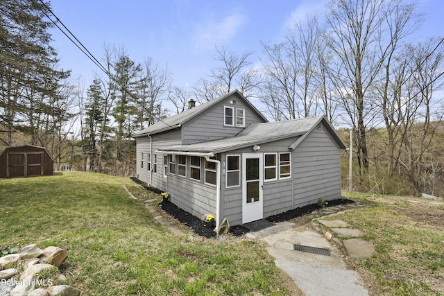 view of home's exterior with a chimney, an outdoor structure, a shingled roof, a storage shed, and a lawn