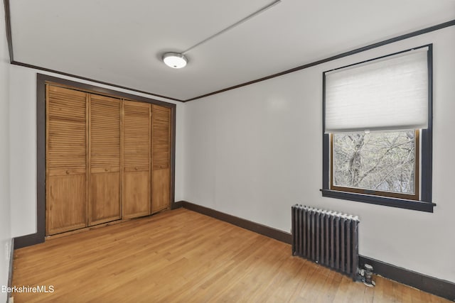 unfurnished bedroom with crown molding, a closet, baseboards, light wood finished floors, and radiator heating unit