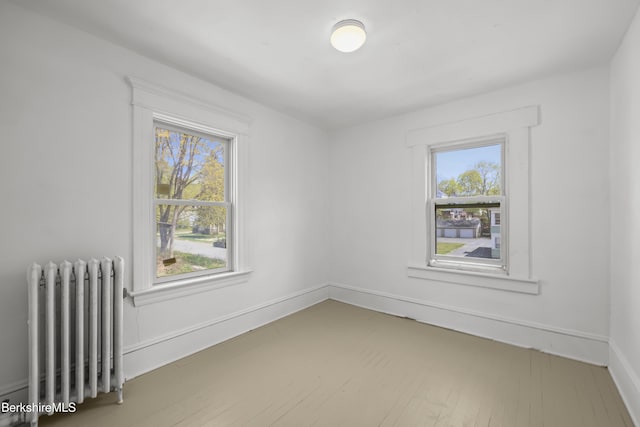 spare room with baseboards, radiator, and wood finished floors