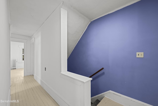 corridor with baseboards, an upstairs landing, radiator heating unit, and wood finished floors