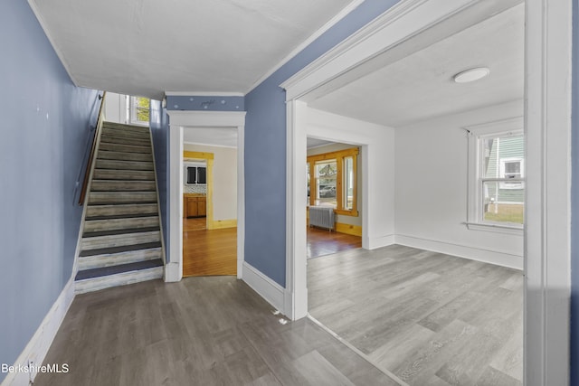 stairs with baseboards, radiator heating unit, crown molding, and wood finished floors