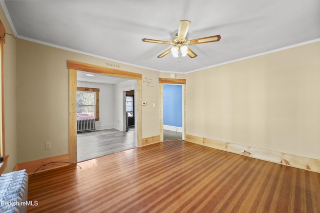 empty room with crown molding, radiator, wood finished floors, baseboards, and ceiling fan