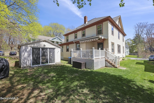 rear view of house featuring a lawn, an outdoor structure, a wooden deck, and a chimney