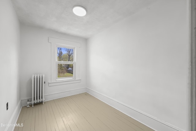 spare room featuring radiator, baseboards, and light wood finished floors