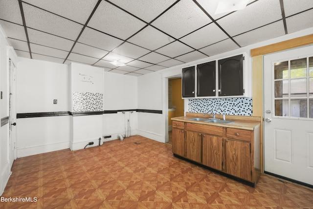 kitchen featuring decorative backsplash, brown cabinets, a sink, light countertops, and a drop ceiling