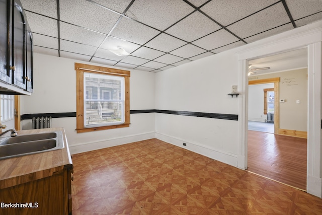 interior space featuring ceiling fan, a sink, butcher block countertops, a paneled ceiling, and baseboards