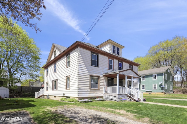american foursquare style home with a porch, an outdoor structure, a front lawn, and a storage shed