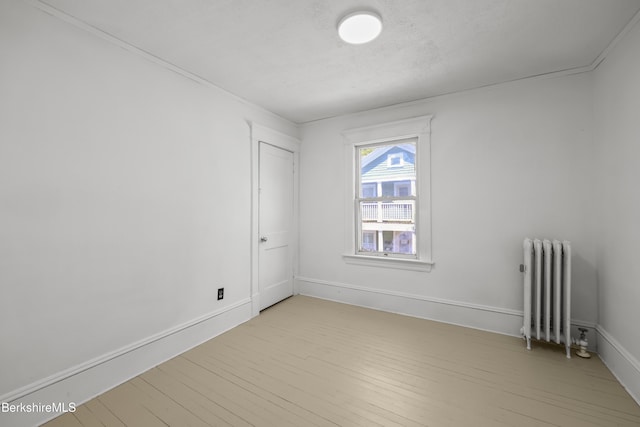 unfurnished room with radiator heating unit, baseboards, and light wood-style flooring