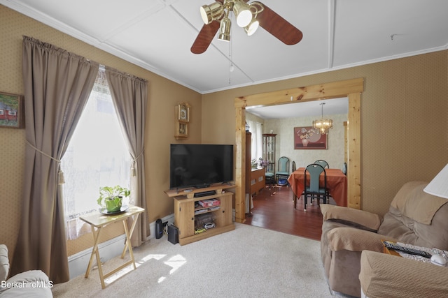 carpeted living room with crown molding, ceiling fan with notable chandelier, and wallpapered walls