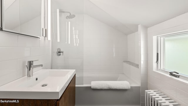 bathroom featuring radiator heating unit,  shower combination, vaulted ceiling, vanity, and tile walls