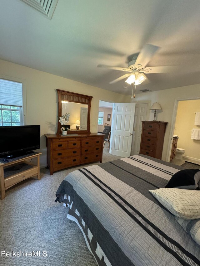 bedroom with ceiling fan, light colored carpet, and ensuite bath