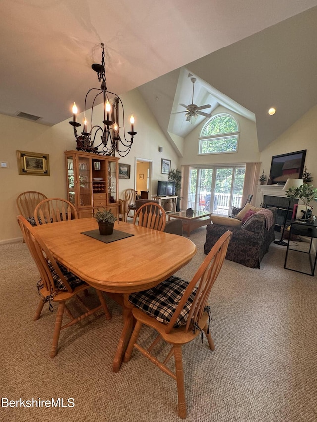 dining room featuring carpet flooring, ceiling fan with notable chandelier, vaulted ceiling, and a tiled fireplace