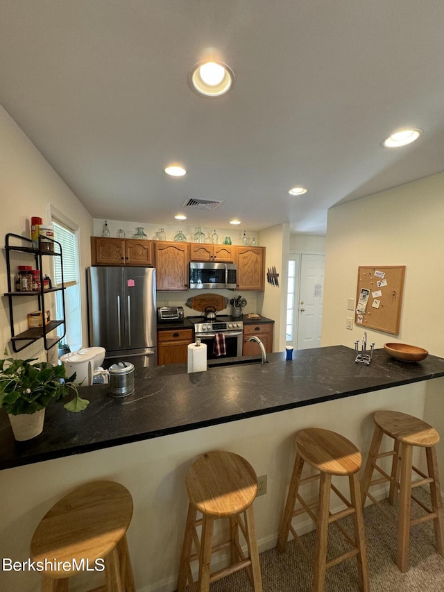 kitchen with a kitchen bar, appliances with stainless steel finishes, carpet floors, and kitchen peninsula