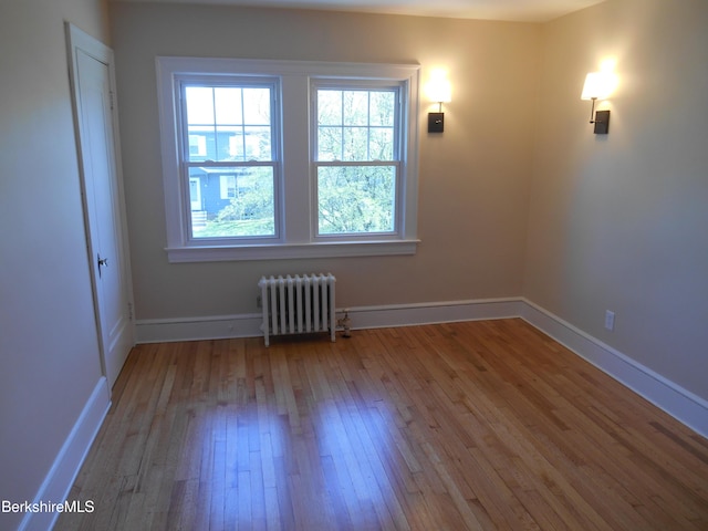 spare room with radiator heating unit, baseboards, plenty of natural light, and hardwood / wood-style flooring