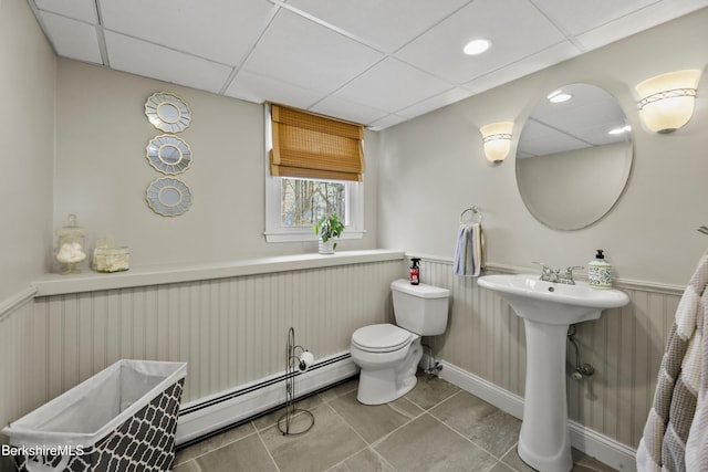 bathroom featuring a drop ceiling, a baseboard radiator, tile patterned floors, and toilet