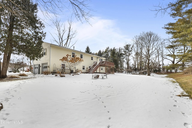 snow covered back of property featuring a garage and a wooden deck