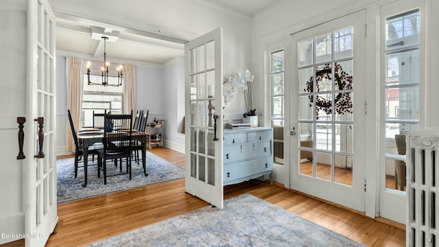 dining room with radiator heating unit, wood finished floors, crown molding, french doors, and a chandelier