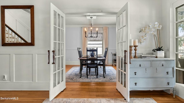 dining room featuring french doors, a wainscoted wall, a decorative wall, an inviting chandelier, and wood finished floors