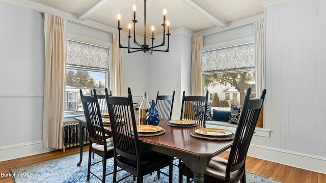 dining space with a textured ceiling, a chandelier, beamed ceiling, and wood finished floors