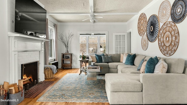 living room with a textured ceiling, a brick fireplace, wood finished floors, and beam ceiling