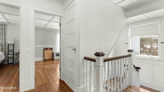 hallway with crown molding, dark wood-type flooring, an upstairs landing, and a decorative wall