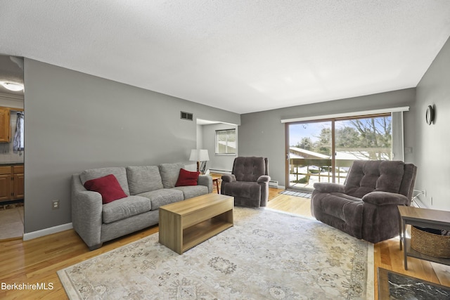 living room with a baseboard radiator, light hardwood / wood-style floors, and a textured ceiling