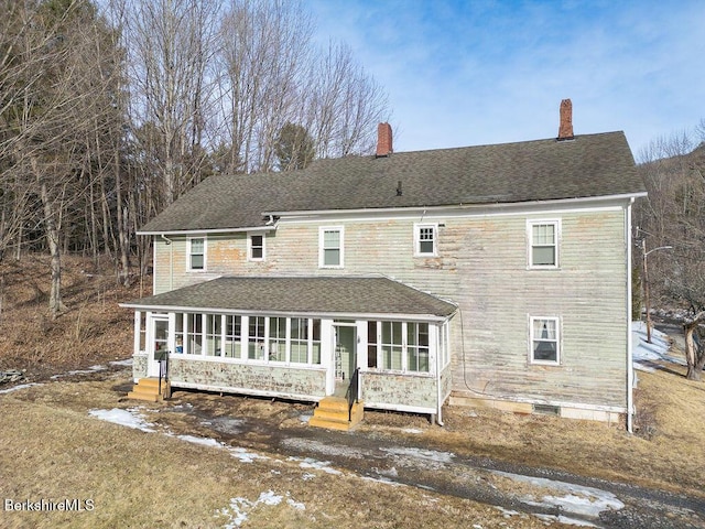 back of property with a sunroom, a shingled roof, and a chimney