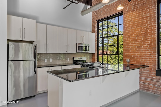 kitchen with sink, a towering ceiling, decorative backsplash, white cabinets, and appliances with stainless steel finishes