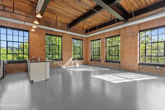 interior space with wooden ceiling, a high ceiling, and brick wall